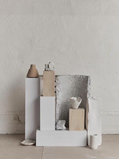 Still life arrangement of ceramic art pieces and geometric pedestals against a textured white wall in a minimalist composition.