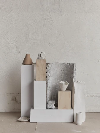 Still life arrangement of ceramic art pieces and geometric pedestals against a textured white wall in a minimalist composition.