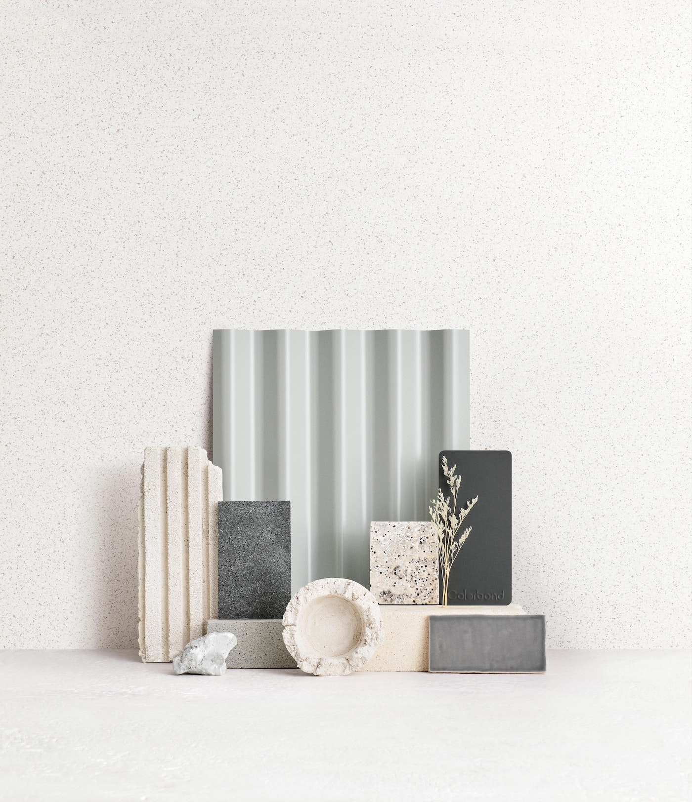Still life composition featuring an arrangement of stone and concrete blocks and a dried floral element against a textured wall backdrop.