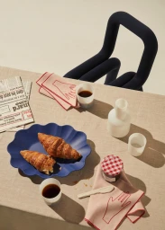 Overhead shot of a table setting with croissants on a blue platter, coffee cups, jam jar, and modern chair styled by Lara Hutton