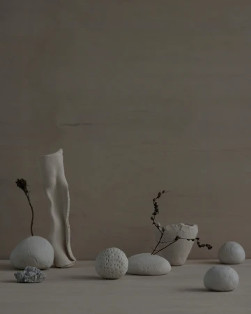 Neutral still life arrangement of textured white ceramic vessels and smooth rounded stones on a wooden surface