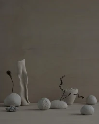 Neutral still life arrangement of textured white ceramic vessels and smooth rounded stones on a wooden surface