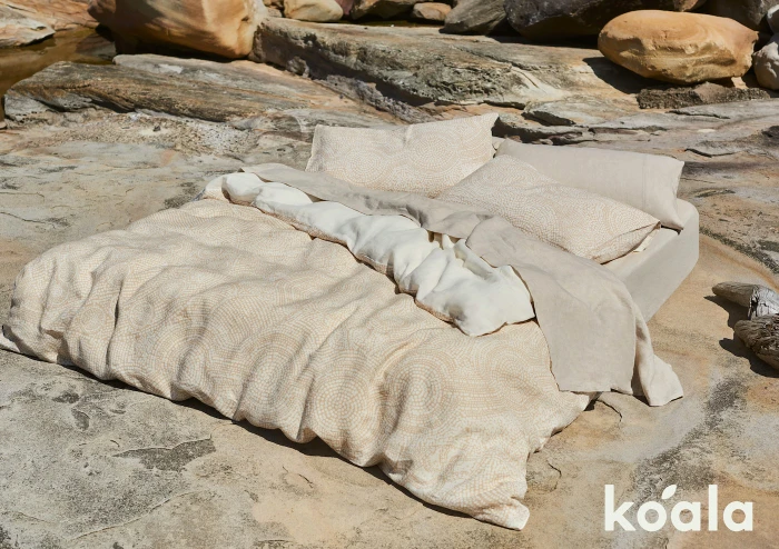 A made bed with patterned duvet and pillows set outdoors on natural stone rocks by Lara Hutton.