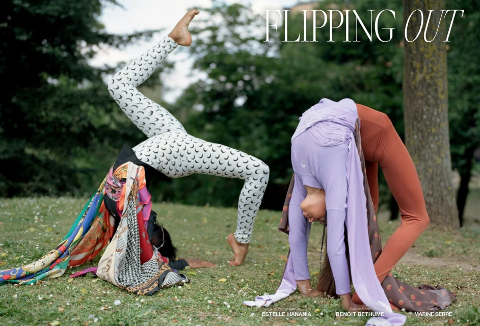 Two flexible women in crescent-moon leggings and exercise clothes perform backbends outdoors in a grassy, wooded setting.