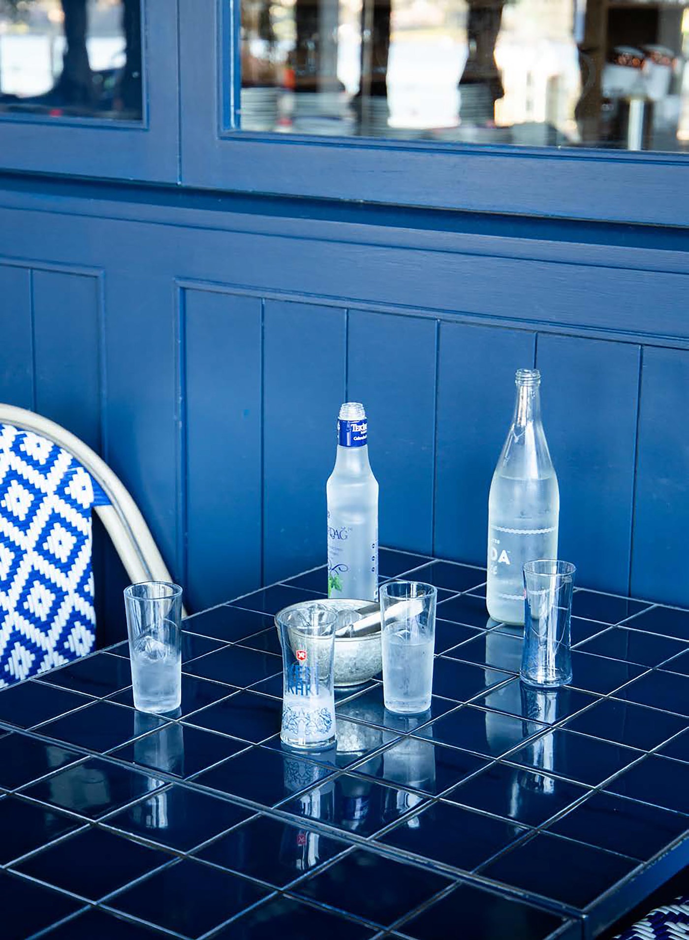 Still life of sparkling water bottles and glasses on a blue-tiled table, with a blue wood panel background, creating a refreshing and clean visual.