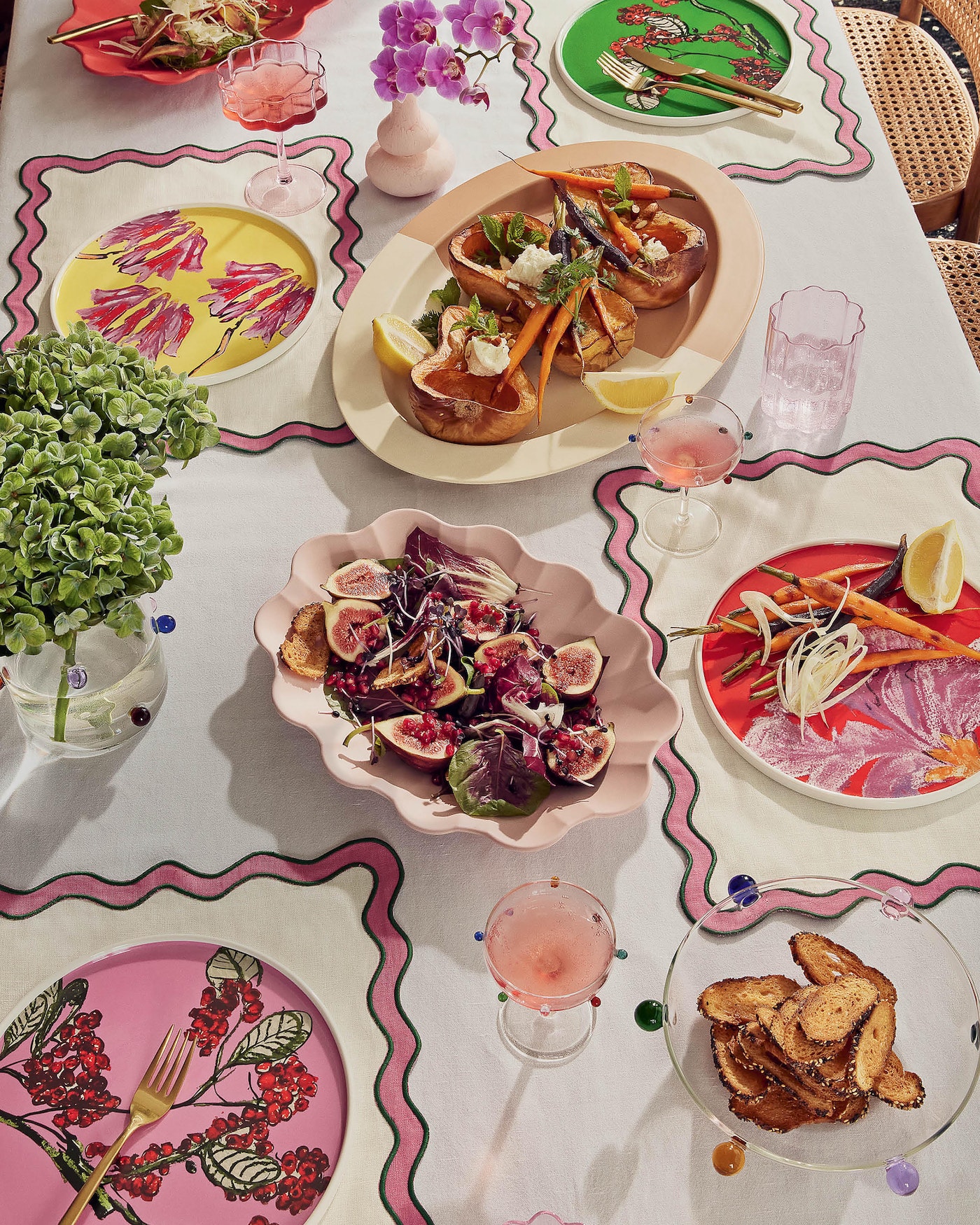 Overhead shot of a beautifully decorated table set with floral plates, cocktails, appetizers, and flower arrangements for a meal.