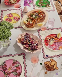 Overhead view of a dining table styled with colourful plates, roasted vegetables, salads, and pink cocktails by Lisa Featherby.