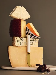 Balanced stack of assorted cheeses on a marble board with a cheese knife styled by Lisa Featherby