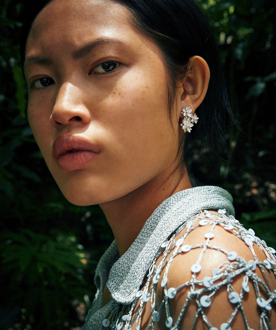 Close-up of an Asian woman wearing flower earrings in a garden setting, illuminated by natural light. Fashion and beauty portrait.