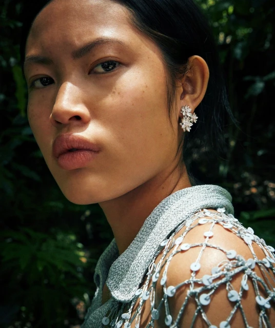 Close-up of an Asian woman wearing flower earrings in a garden setting, illuminated by natural light. Fashion and beauty portrait.