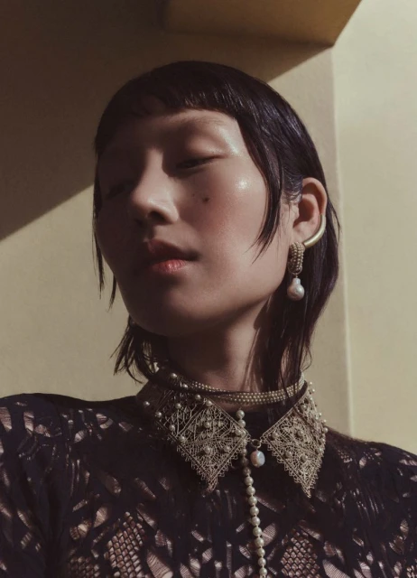 Close up portrait of a woman with dark hair wearing an ornate pearl collar necklace and pearl earrings