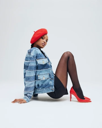 A fashionable woman in a denim jacket, red beret, and heels poses in a studio setting. The image highlights clothing and style.
