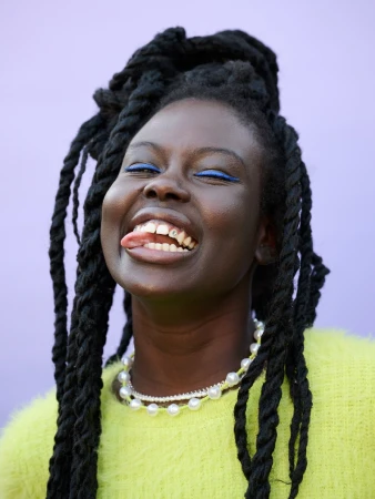 Close-up portrait of a smiling adult woman with dark skin and black hair wearing a chartreuse sweater and double pearl necklace. 
