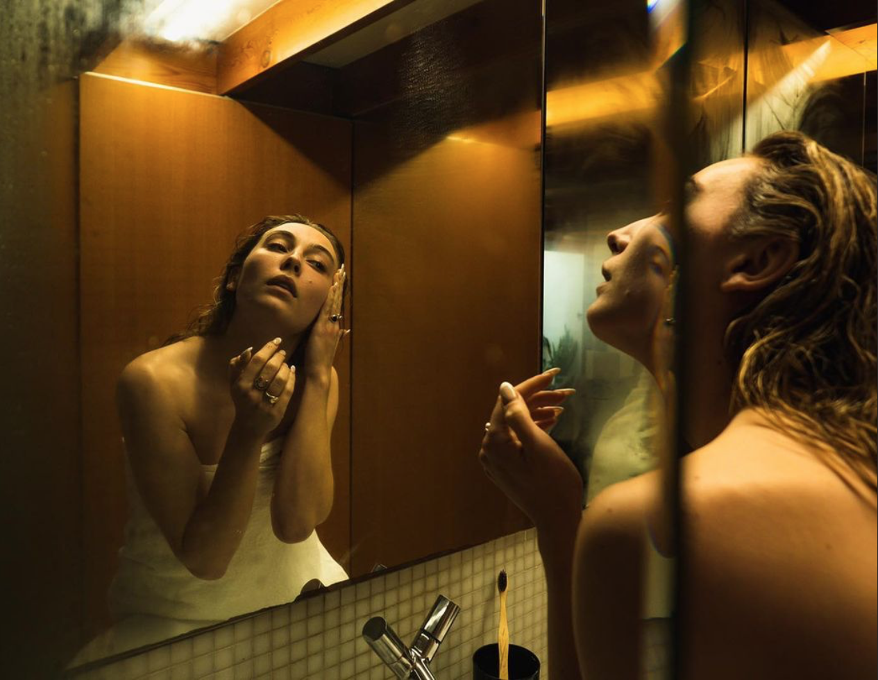 Woman with wet hair wrapped in a towel looking in the mirror in warm bathroom light with a toothbrush in view. Beauty concept.