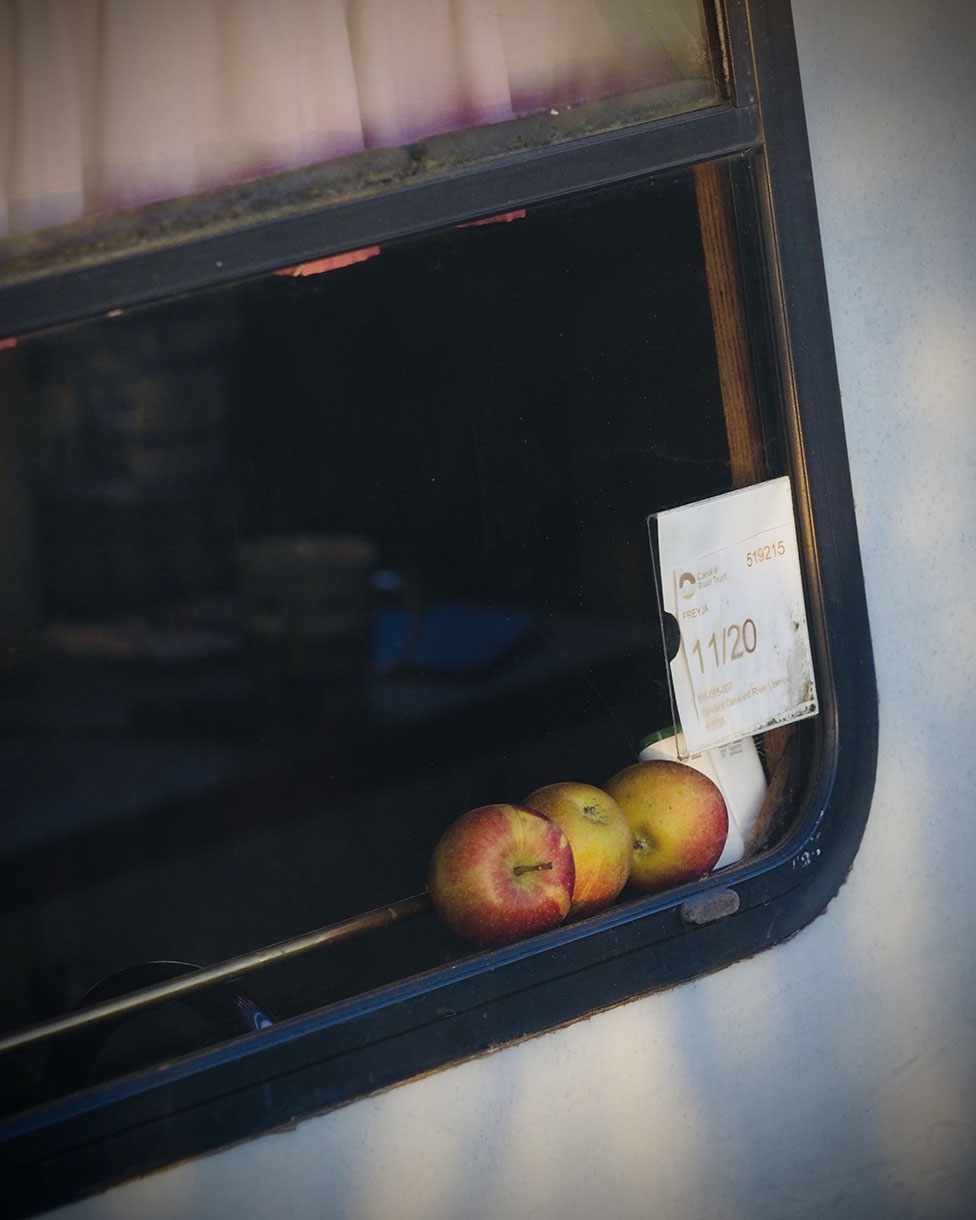 Three apples sit on the inside ledge of a camper van window, with light coming in from the window and a tag on the glass.