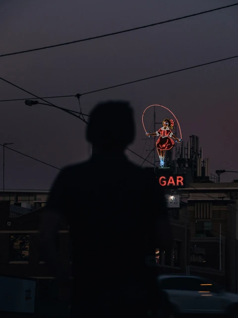 Person in shadow near neon sign of a girl jumping rope at night, dark and atmospheric, with building and wires in the background.