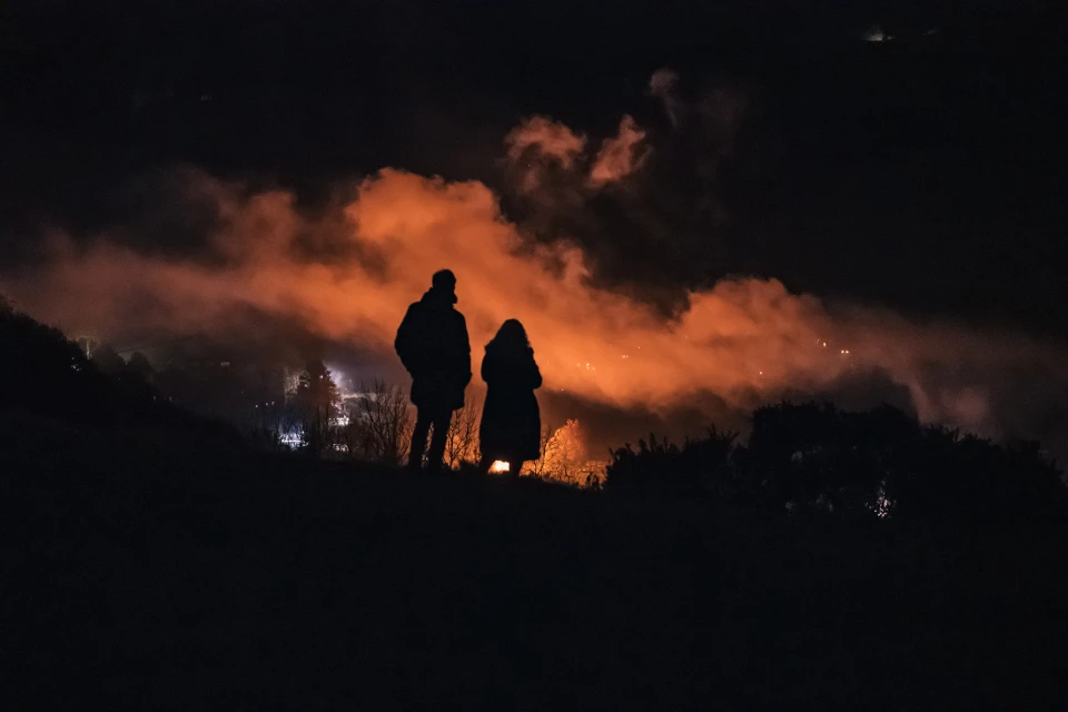 Two figures silhouetted against a night sky, viewing an atmospheric orange cloud, creating a dramatic and mysterious outdoor scene.