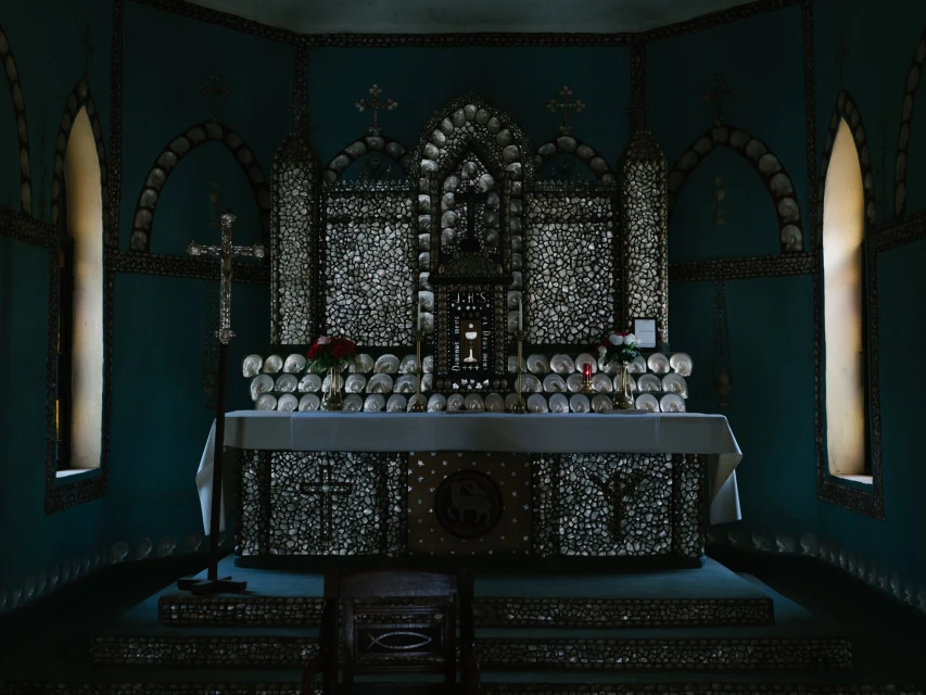 Interior view of a chapel featuring an altar, crucifix, and decor with numerous seashells and floral arrangements, illuminated by natural light.