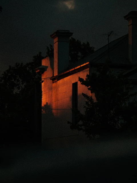 Exterior view of a building at night, featuring a facade illuminated by warm light, with trees and foliage surrounding the structure.
