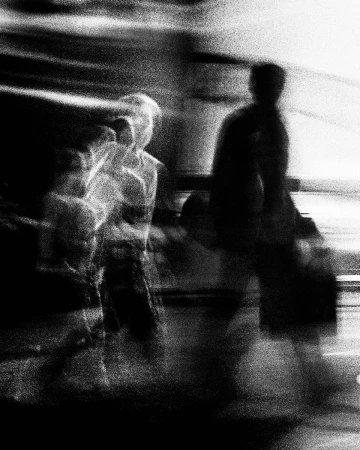 High-contrast monochrome long-exposure photograph of blurred figures walking on a city street by Andy Hatton.