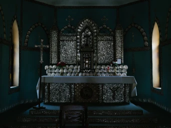 Interior view of an ornate chapel altar decorated entirely with iridescent seashell mosaics and a central crucifix.