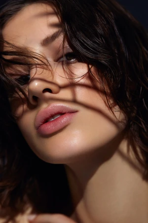 Close-up portrait of a woman with dark hair cast in striped shadows by Daniella Rose