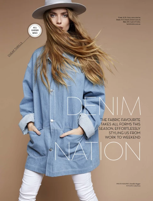 Fashion editorial shot of a woman in a denim jacket, white pants, and a hat against a tan background in a photo studio setting.