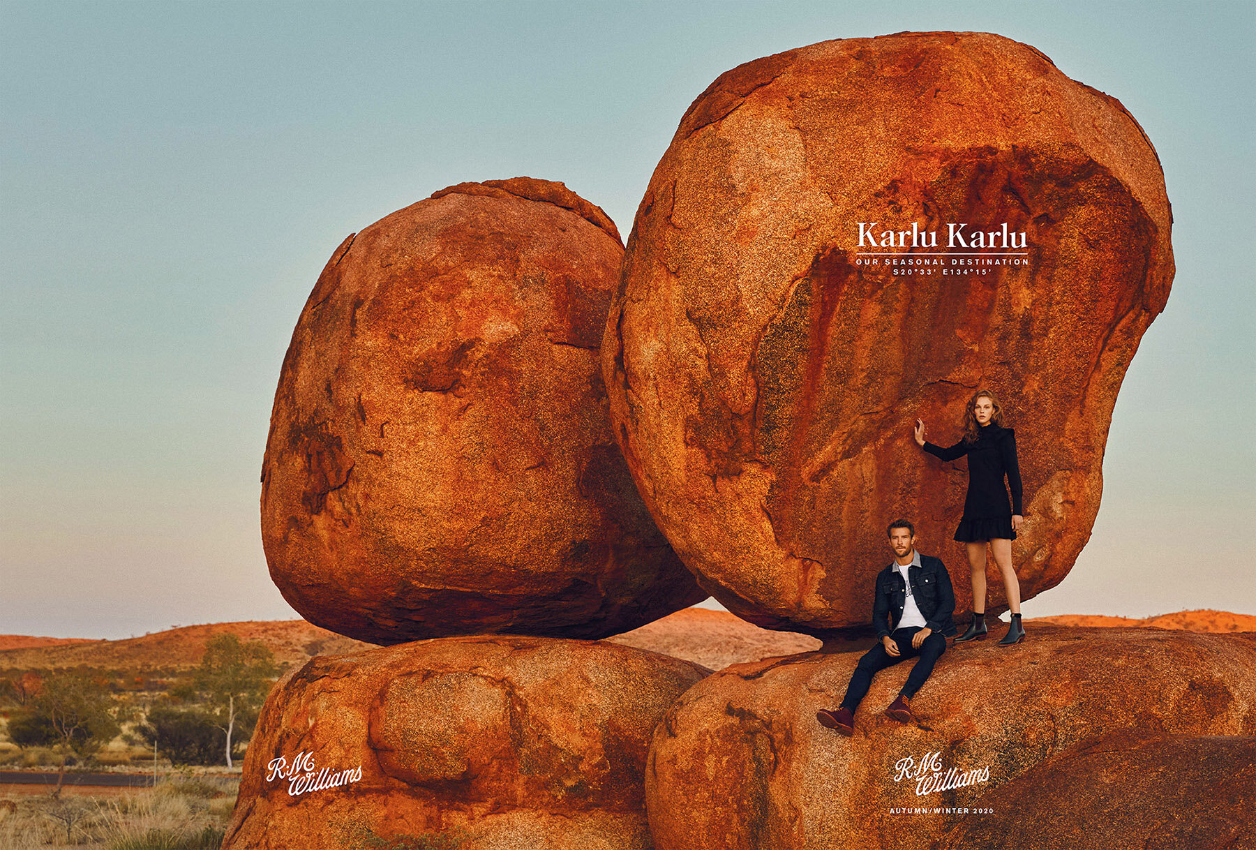 Fashion editorial shot of a man and woman posing on naturally stacked rocks in the Australian outback with clear blue sky in the background.