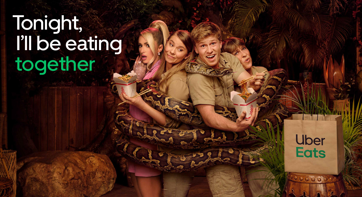 Uber Eats ad featuring four people with an enormous snake wrapped around them eating noodles out of Chinese takeout containers.