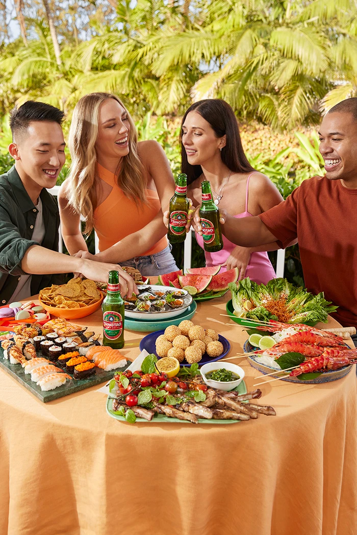 Four friends gathered around an outdoor table laden with food and green glass bottles, styled by Jerrie Joy Redman Lloyd.
