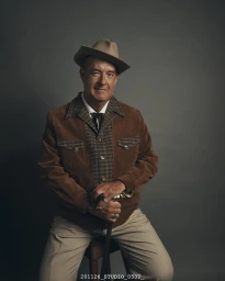 Portrait of Tom Hanks wearing a brown corduroy jacket, fedora hat, and holding a walking cane, photographed by Hugh Stewart.