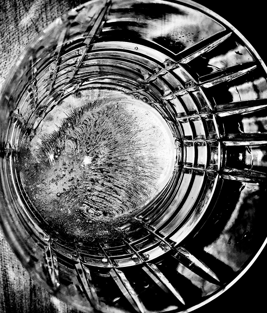 Close-up view looking inside a clear glass, with light refracting through the crystal-cut design and illuminating the abstract liquid patterns.
