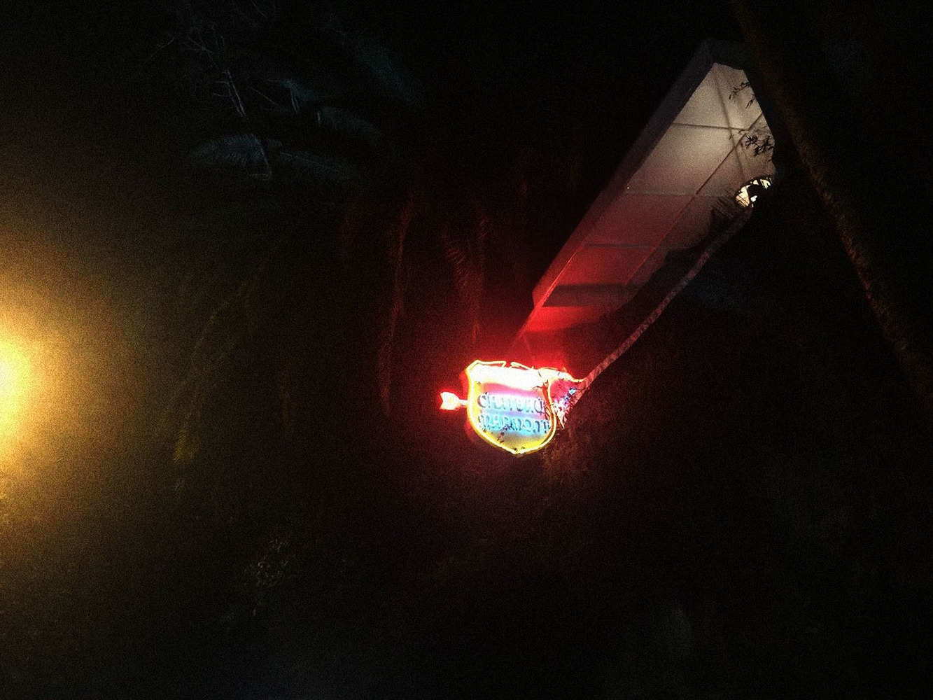 Illuminated sign for Chowder Pot Pub restaurant at night with dark trees and an overhanging roof structure.