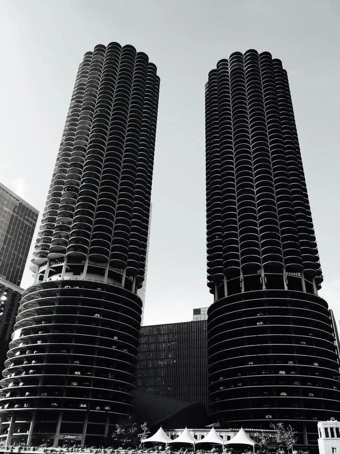 Monochrome low angle view of two distinctive cylindrical high rise towers against a bright sky, captured by Jordan Doner.