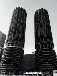 Monochrome low angle view of two distinctive cylindrical high rise towers against a bright sky, captured by Jordan Doner.