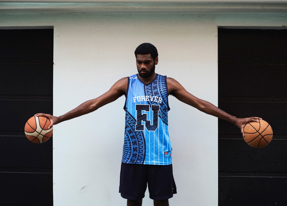 A man in a blue basketball jersey with the word 'FOREVER' and 'FJ' holds a basketball in each hand in front of a neutral background.