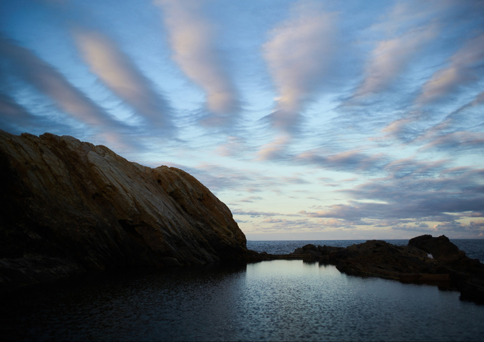 Scenic view of coastal rock formations with tide pools and striking cloud patterns in a natural landscape under a blue sky.