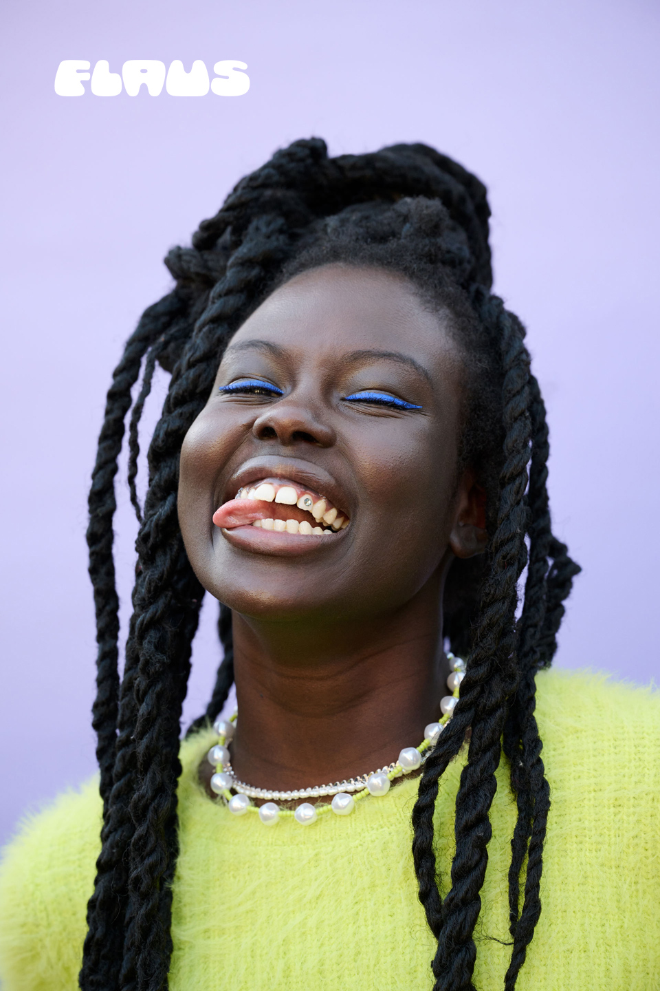 Smiling Black woman with braided hair, pearl necklace, and bright green top against a lavender background, sticking out her tongue.