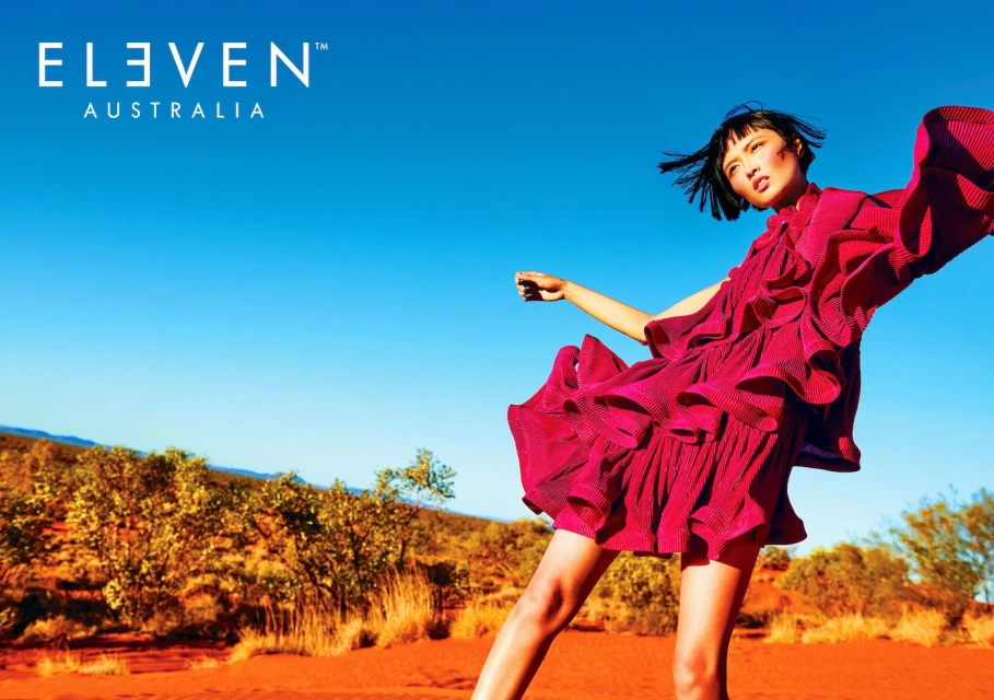 A fashionable woman in a pink dress poses in a desert landscape against a clear blue sky, showcasing style and natural beauty.