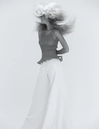 Monochrome portrait of a woman with voluminous textured hair wearing a sleeveless top and white trousers