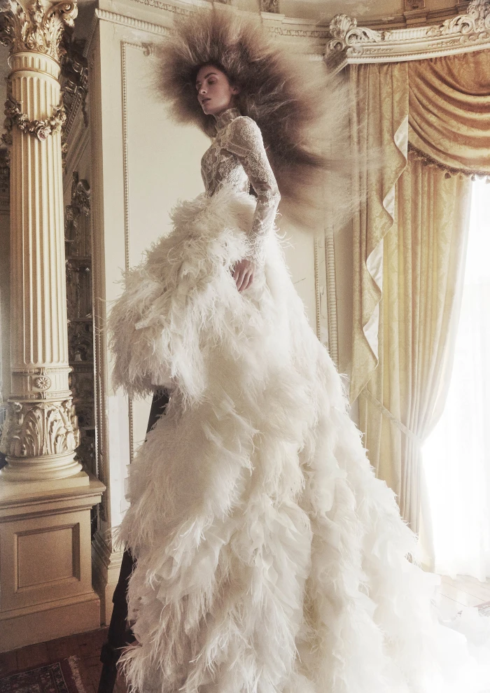 Model with voluminous feathered hair wearing a dramatic white lace gown standing inside an ornate historic room in Sydney