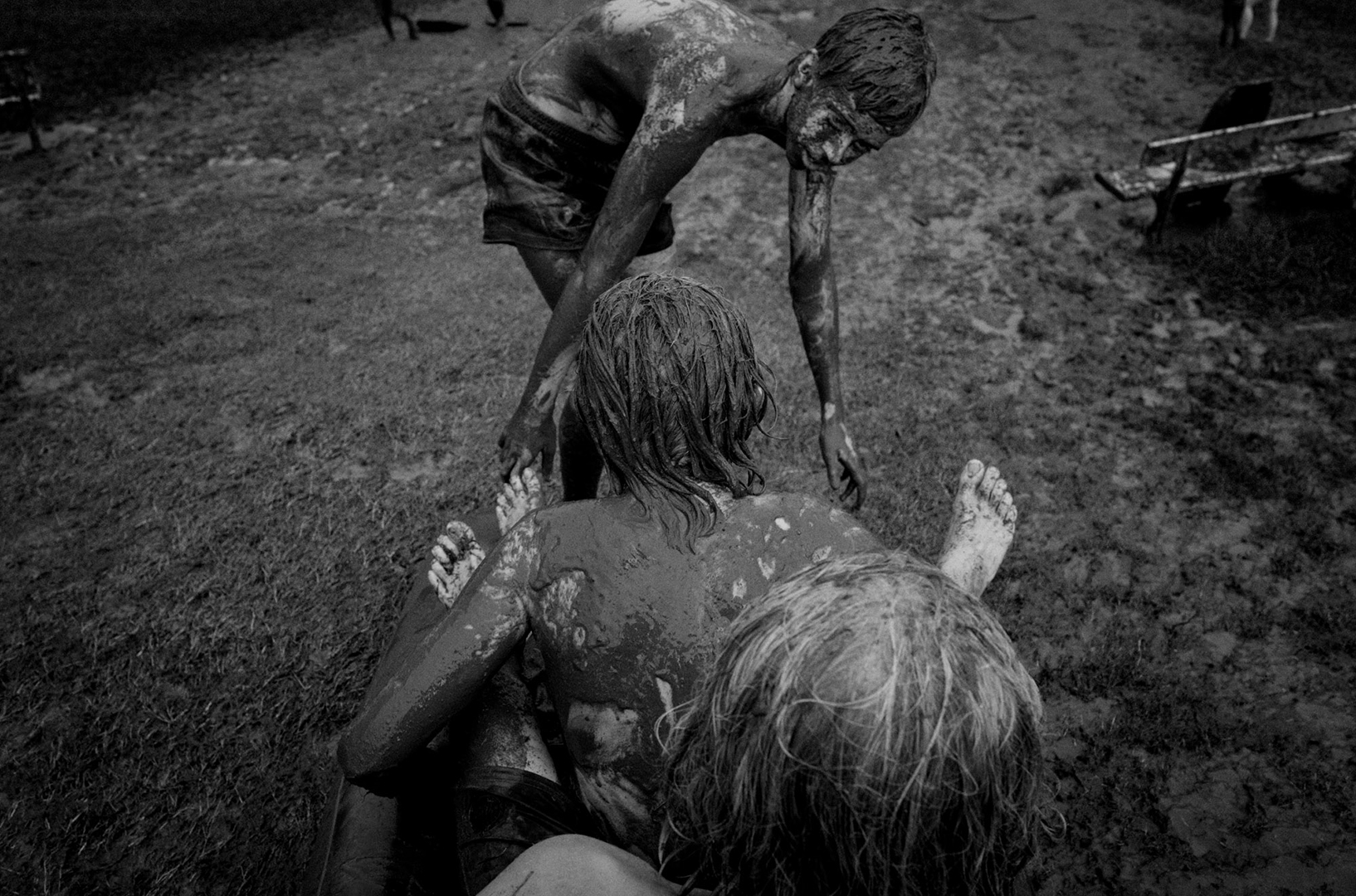 Three people covered in mud, one standing, two prone on the ground, creating a striking image of nature and physicality.