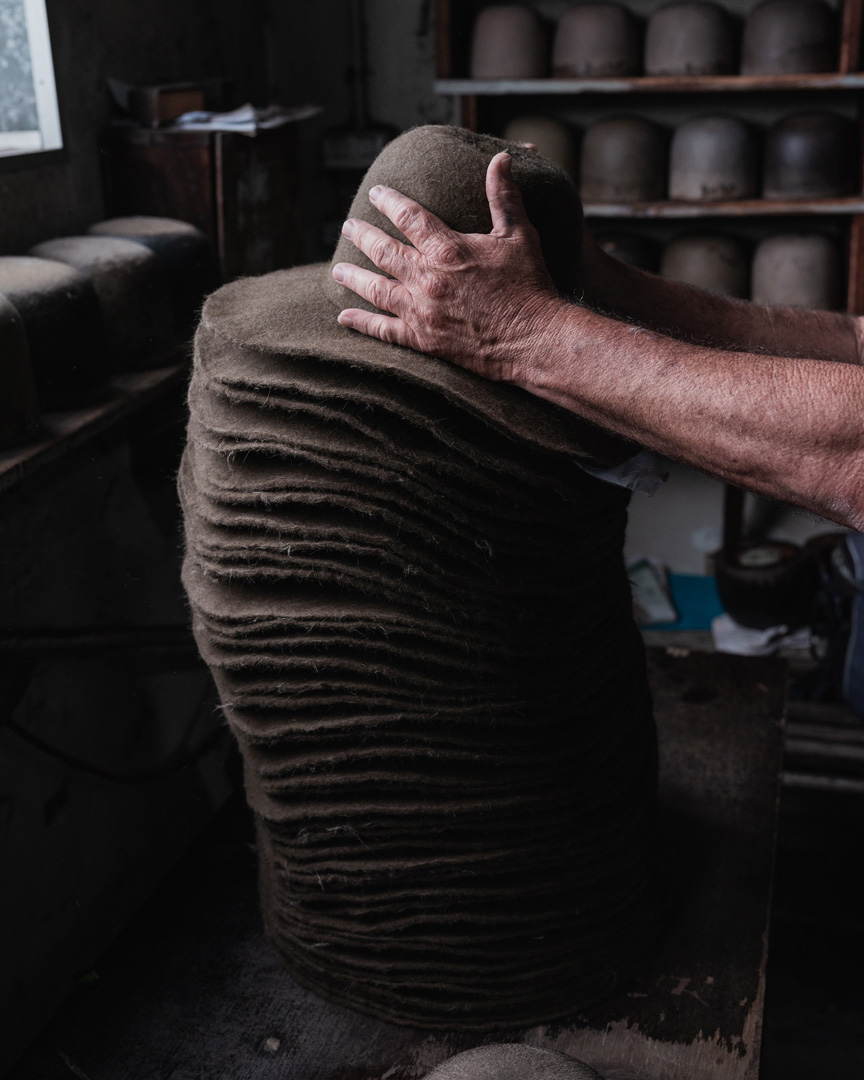 Stack of felt hats being shaped in a workshop by a person's hands, showing the texture and craftsmanship involved in hat making.