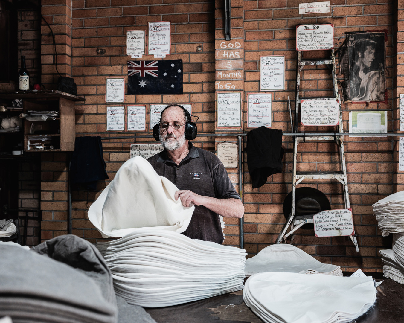 Man with a beard folds fabric in an indoor industrial setting with brick walls and handwritten notes and posters hanging in the background.