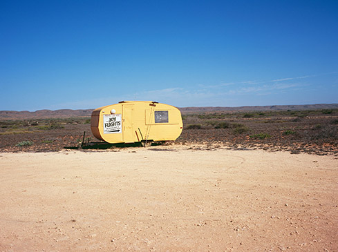 Yellow transport trailer in a desert landscape under a clear blue sky with sparse vegetation, featuring ground and distant low hills.