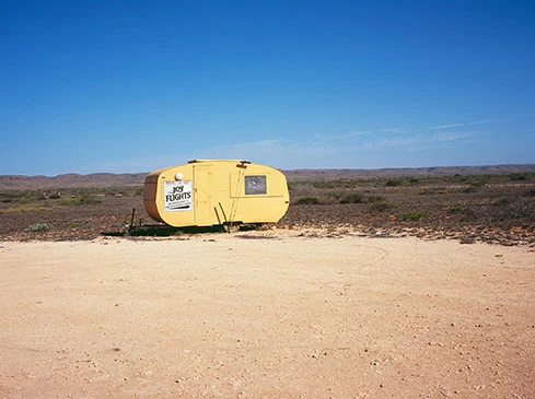 Yellow transport trailer in a desert landscape under a clear blue sky with sparse vegetation, featuring ground and distant low hills.