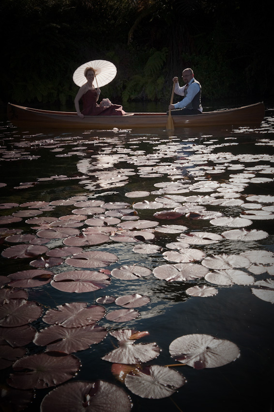 Romantic moment: A couple glides on a wooden canoe across a lake filled with lily pads in soft, natural lighting, exuding a peaceful atmosphere.