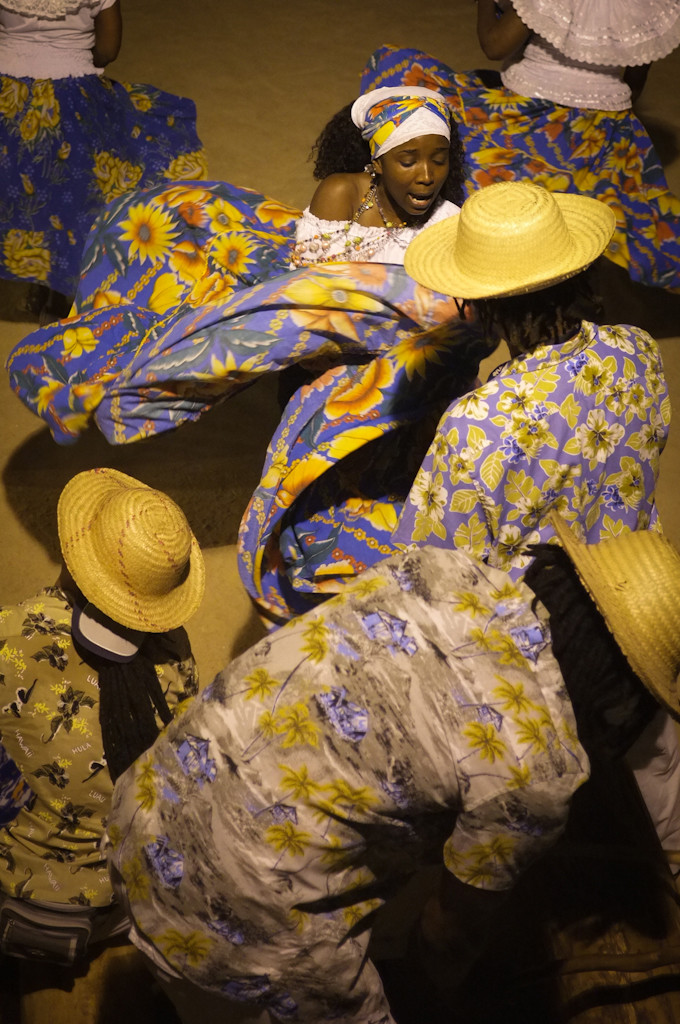 Group of people in colorful floral clothes and straw hats performing a traditional dance, celebrating culture outdoors at night.