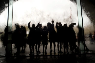 Silhouettes of people standing behind a cascading water wall with their hands raised