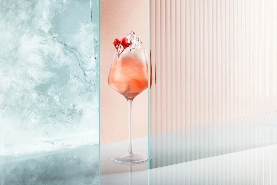 A refreshing beverage presentation featuring an aperol spritz-like drink with ice and floral garnish, set against textured backdrops.